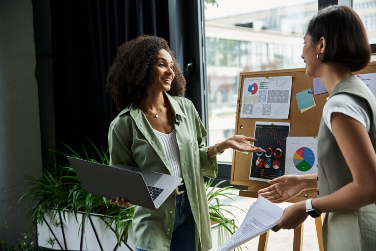 A lesbian couple work in an office, discussing charts.