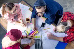 Quatre personnes rassemblées autour d’une table, travaillant sur des plans et des nuanciers de couleurs, en pleine discussion.