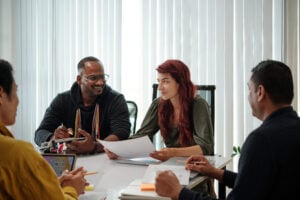 Groupe de collègues souriants en pleine discussion autour d’une table de réunion.