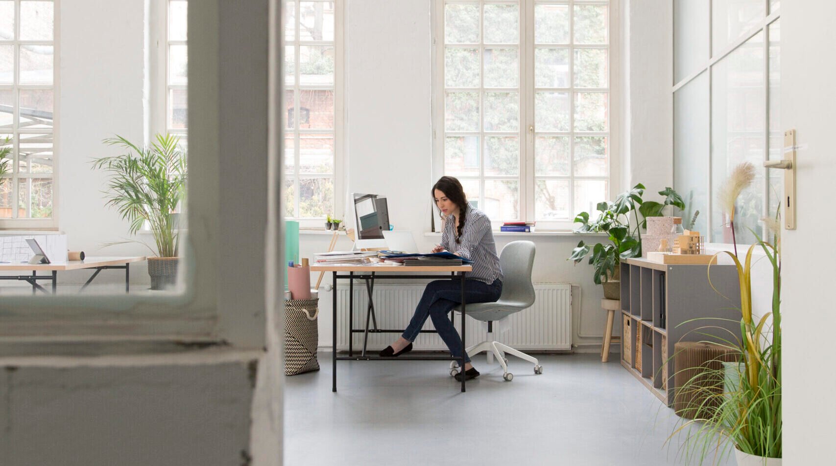 Femme seule travaillant dans un bureau lumineux et épuré, entourée de plantes vertes.