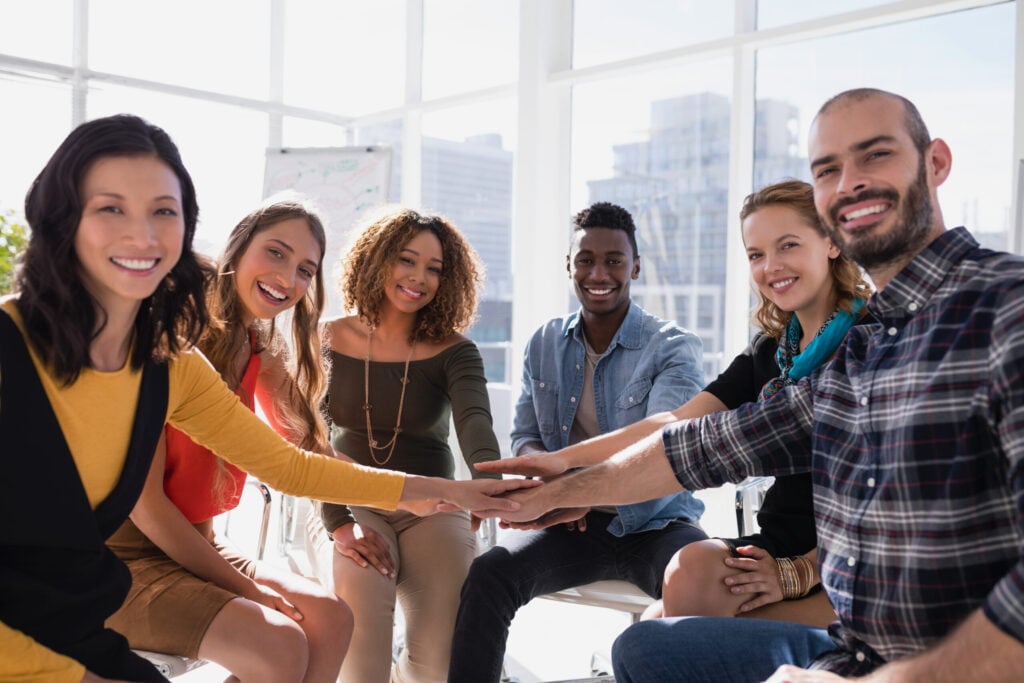 Groupe diversifié de collègues réunis, mains au centre, souriants et enthousiastes.