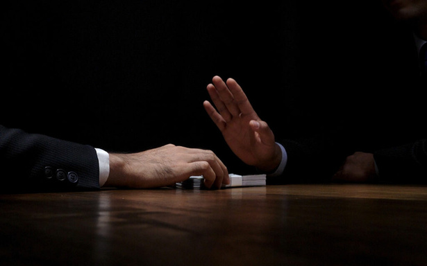 Une main refuse un billet glissé sur une table
